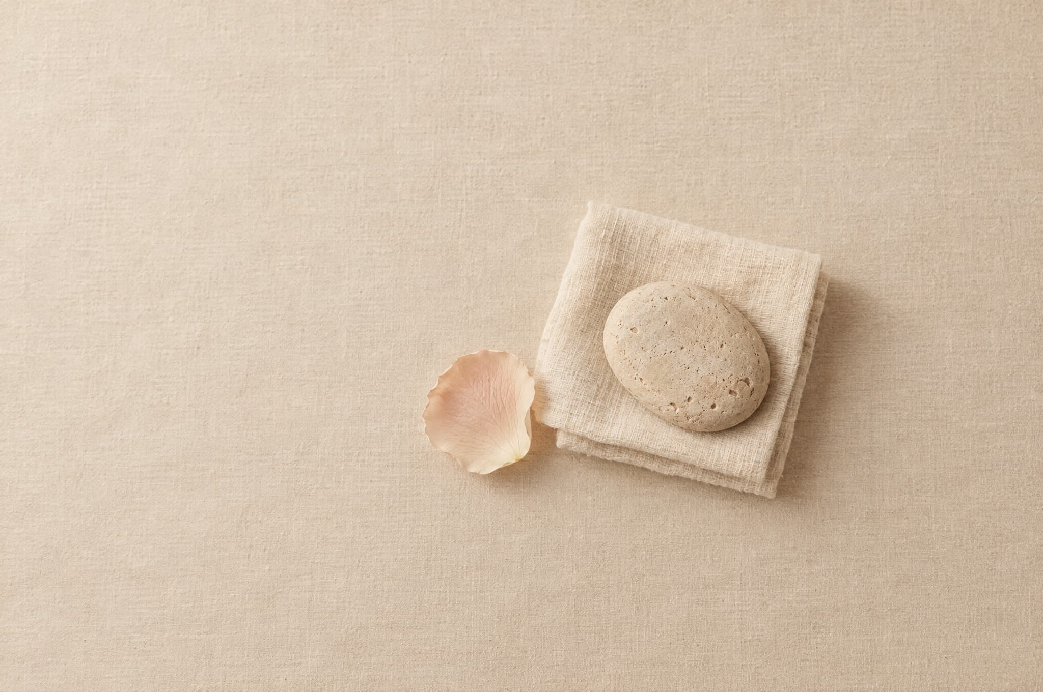 A folded muslin cloth with a smooth pale stone and a blush rose petal